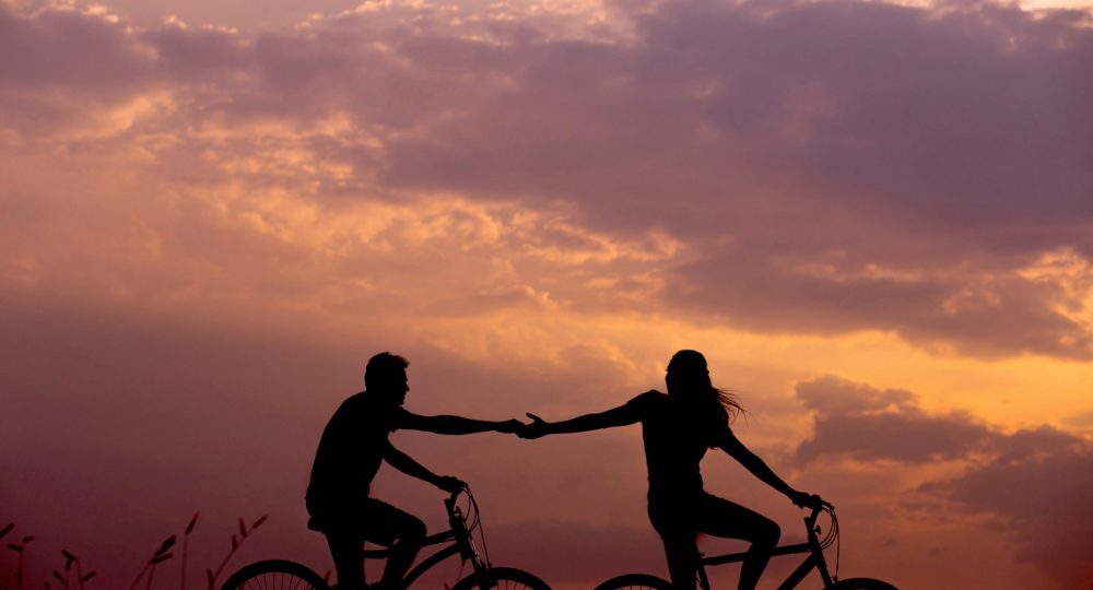 woman on bike reaching for man's hand behind her also on bike