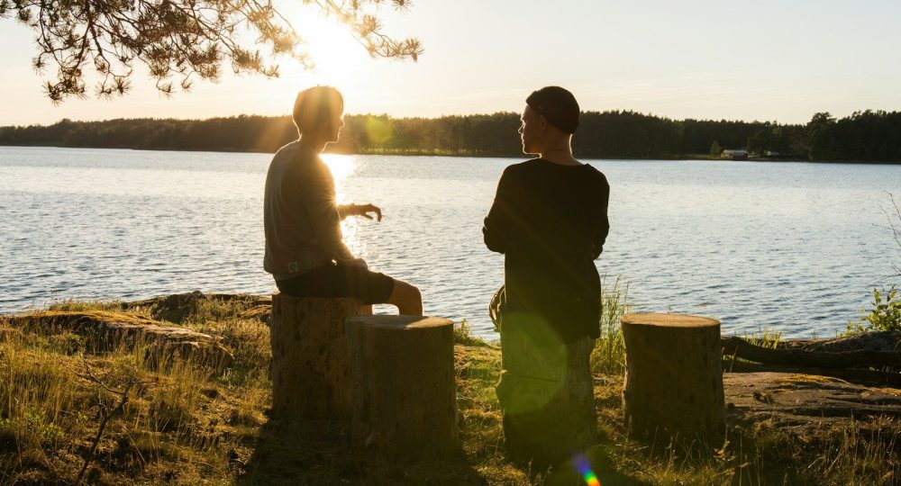 man in black jacket standing beside body of water during sunset