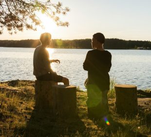 man in black jacket standing beside body of water during sunset